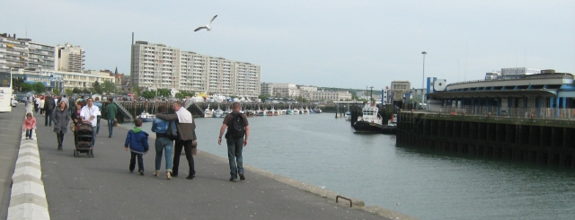 the port at boulogne-sur-mer, a big open strech of water lined with hotels and tall buildings and people walking around